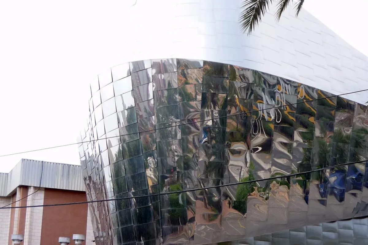 Polished mirror-steel panels on the curved corner of Benidorm Palace, reflecting palms and the street