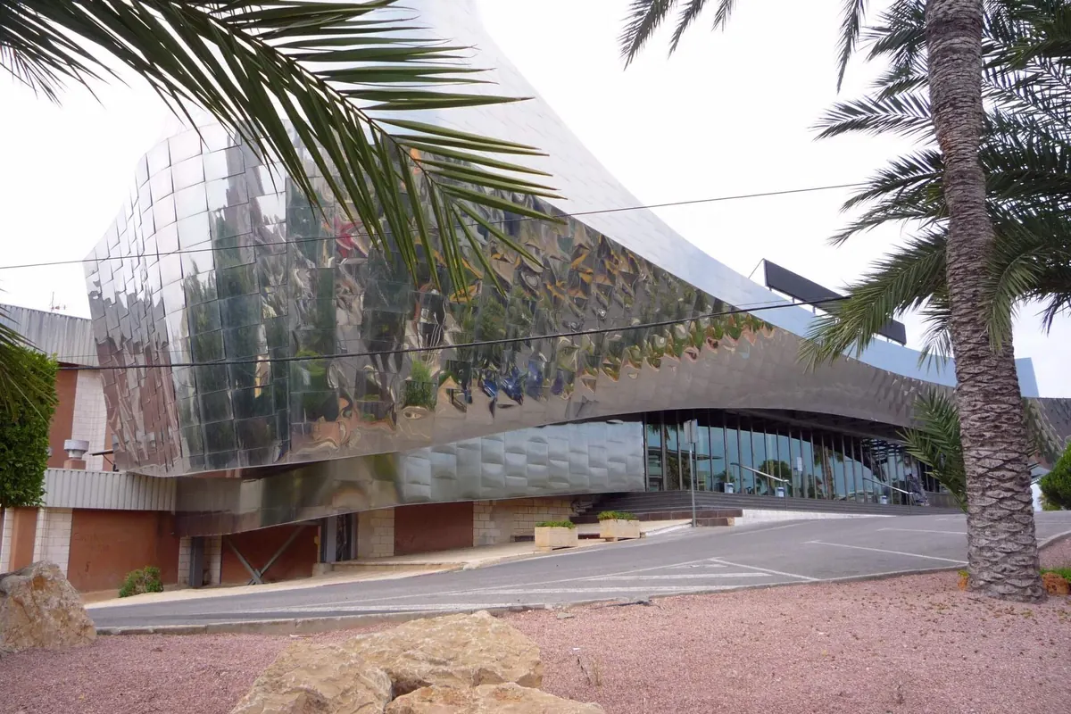 The curved corner of Benidorm Palace, clad in polished mirror steel, with palm leaves and a road in front