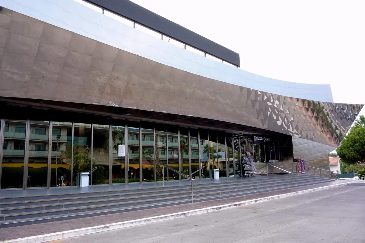The curved mirror-steel facade of Benidorm Palace above a wide flight of steps and the glass entrance doors