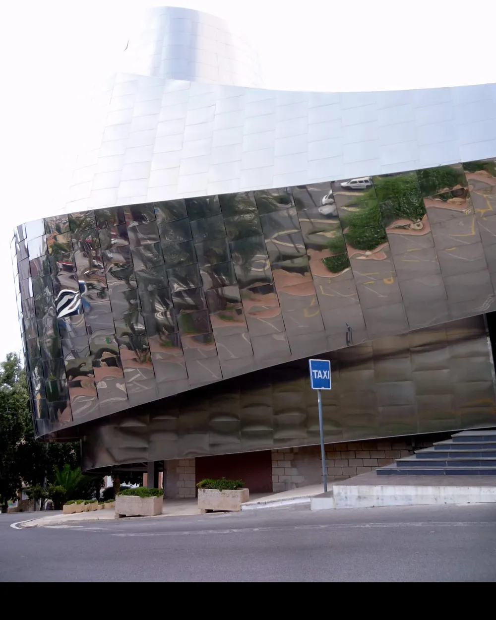 The curved wall of Benidorm Palace rising over a street corner, with a blue taxi sign beside the steps