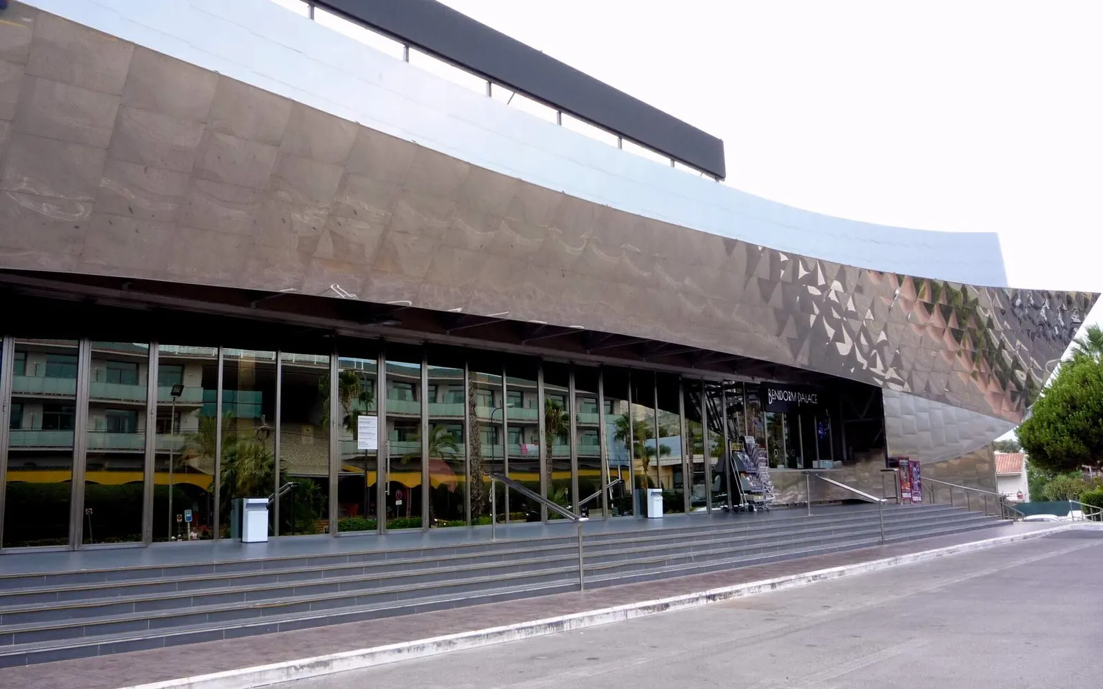 The curved front of Benidorm Palace, clad in polished metal, above a wide flight of steps and glass doors